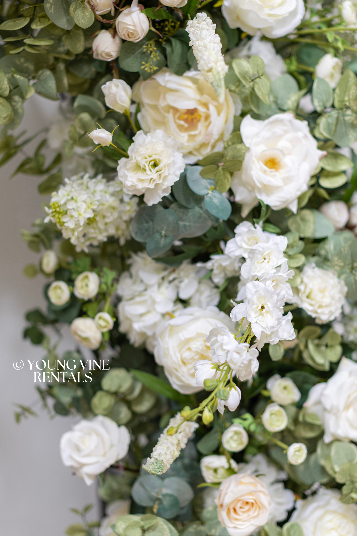 Close-up detail shot of lush, romantic wedding floral arbor studded with an abundance of ivory and white flowers and various types of eucalyptus foliage, styled on a black filigree arch frame.