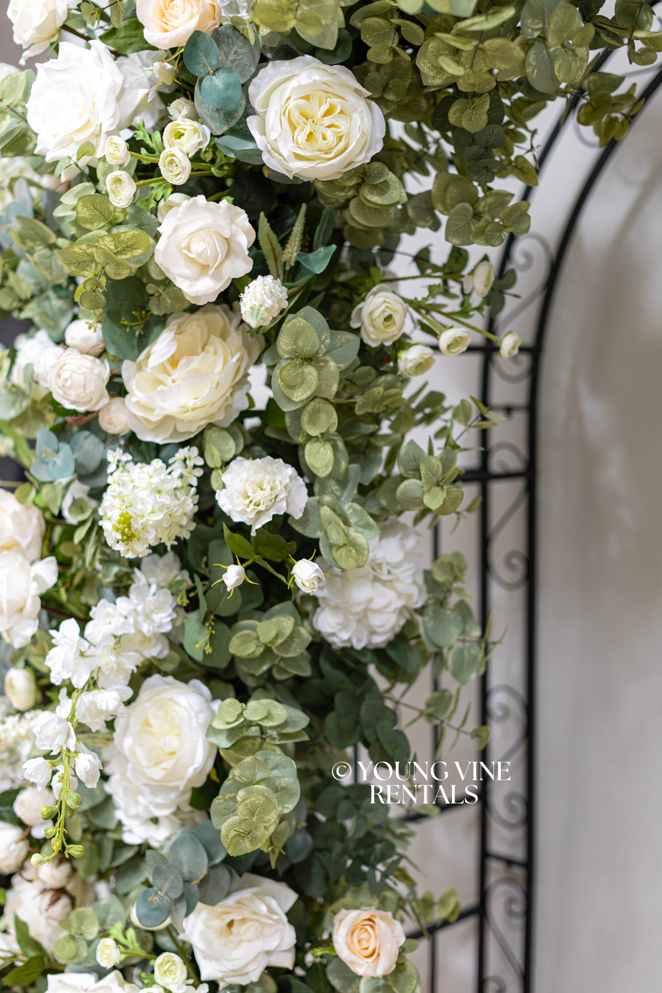 Close-up detail shot of lush, romantic wedding floral arbor studded with an abundance of ivory and white flowers and various types of eucalyptus foliage, styled on a black filigree arch frame.